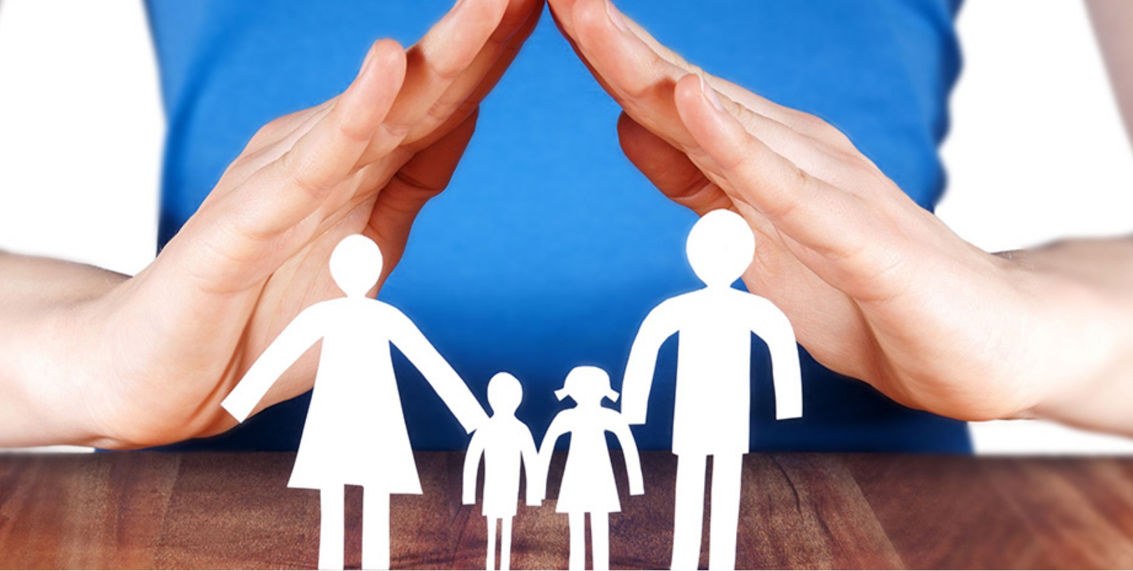 Dłonie ułożone w kształt dachu chronią papierowe sylwetki rodziny: dwoje dorosłych i dwoje dzieci, symbol bezpieczeństwa i wsparcia dla rodziny